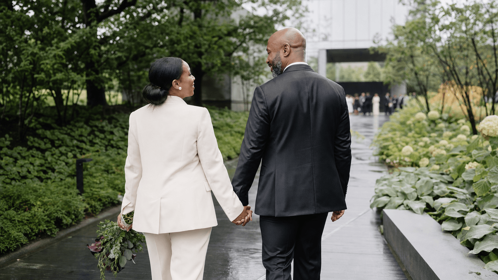 A newly married couple walking hand in hand through a garden